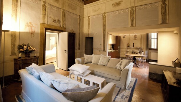 A spacious living room with a high ceiling, a sofa set, a coffee table, and a dining area with a chandelier.