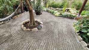 A garden with a pebble path, a hammock, and various plants.
