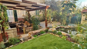 A covered patio with outdoor furniture, a small pond, and a well-maintained garden.