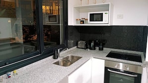 Eine moderne Küche mit Granit Arbeitsplatte, Edelstahlspüle, weißen Schränken, einer schwarzen Spritzschutzwand, einer Mikrowelle und einem Backofen.