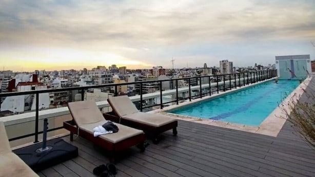 Ein Poolbereich auf dem Dach mit Liegestühlen und Blick auf die Stadt.