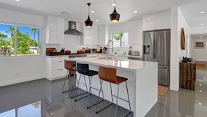 A modern kitchen with white cabinetry, stainless steel appliances, and a central island with bar stools. - Spectacular Luce  Desert Escape-  Oversized Resort setting + golf cart (Palm Desert)
