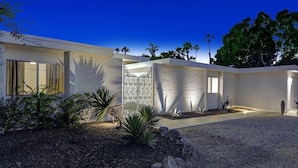 A modern house with a white exterior, a decorative metal gate, and a gravel driveway. - Spectacular Luce  Desert Escape-  Oversized Resort setting + golf cart (Palm Desert)