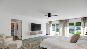 A modern bedroom with a large bed, a flat-screen TV, and a view of the outdoors. - Spectacular Luce  Desert Escape-  Oversized Resort setting + golf cart (Palm Desert)