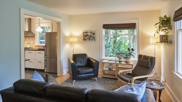 A modern living room with a black leather sofa, two leather chairs, a small wooden table, and a window with a view of greenery. - The Madrona House!
Freshly renovated bungalow / detached studio/office space. (Portland)