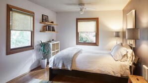A bedroom with a bed, two windows with blinds, a ceiling fan, a bedside lamp, a small wooden stool, and a potted plant. - The Madrona House!
Freshly renovated bungalow / detached studio/office space. (Portland)