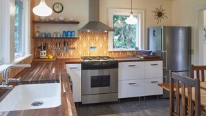 A modern kitchen with a stainless steel stove, oven, and refrigerator, wooden countertops, and a window with a view of trees. - The Madrona House!
Freshly renovated bungalow / detached studio/office space. (Portland)