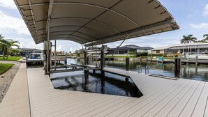 Een kade aan het water met een overdekte looppad, een boot en een jachthaven met huizen op de achtergrond.