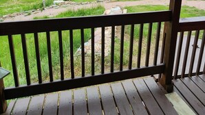 A wooden deck with a view of a green field and trees under a cloudy sky. - Teeny Home in the Black Hills! (Custer)