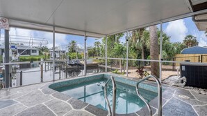 An indoor swimming pool with stone flooring, metal railings, and a view of boats and palm trees outside. - Port Charlotte Private Splash Pool with Canal 3 bedroom Home (Port Charlotte)