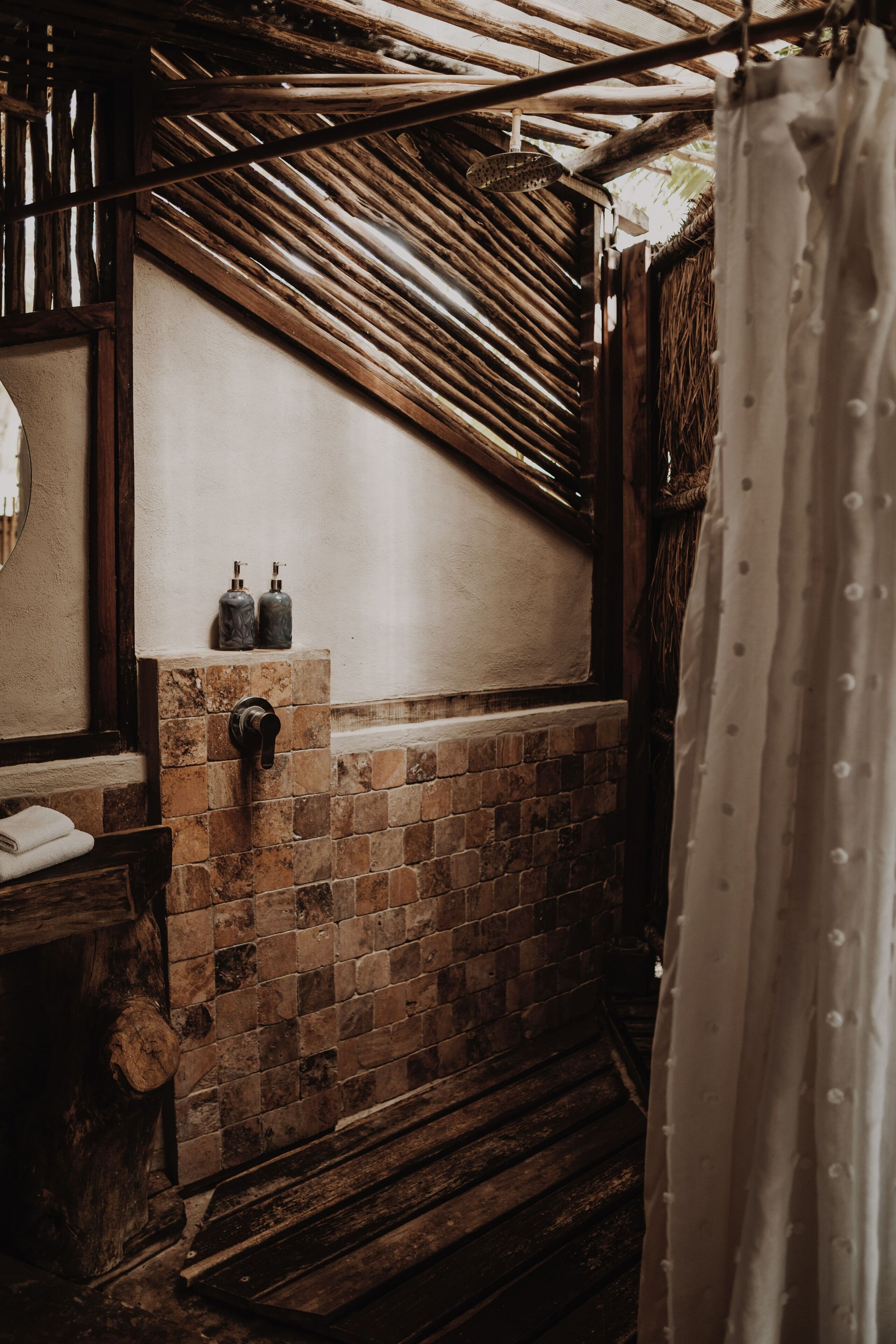Un baño rústico con pared de ladrillo, vigas de madera y cortina de ducha.