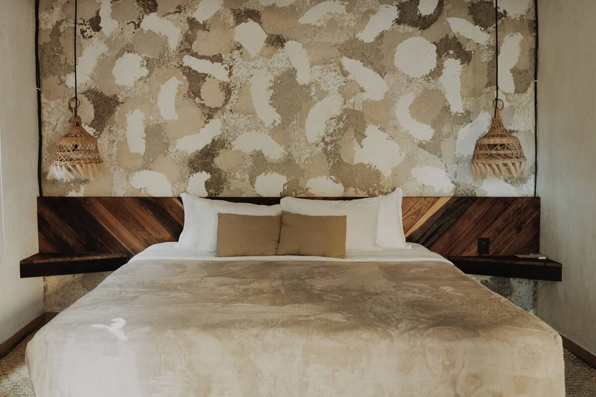 Un dormitorio con una cama grande, cabecera de madera y dos lámparas colgantes.