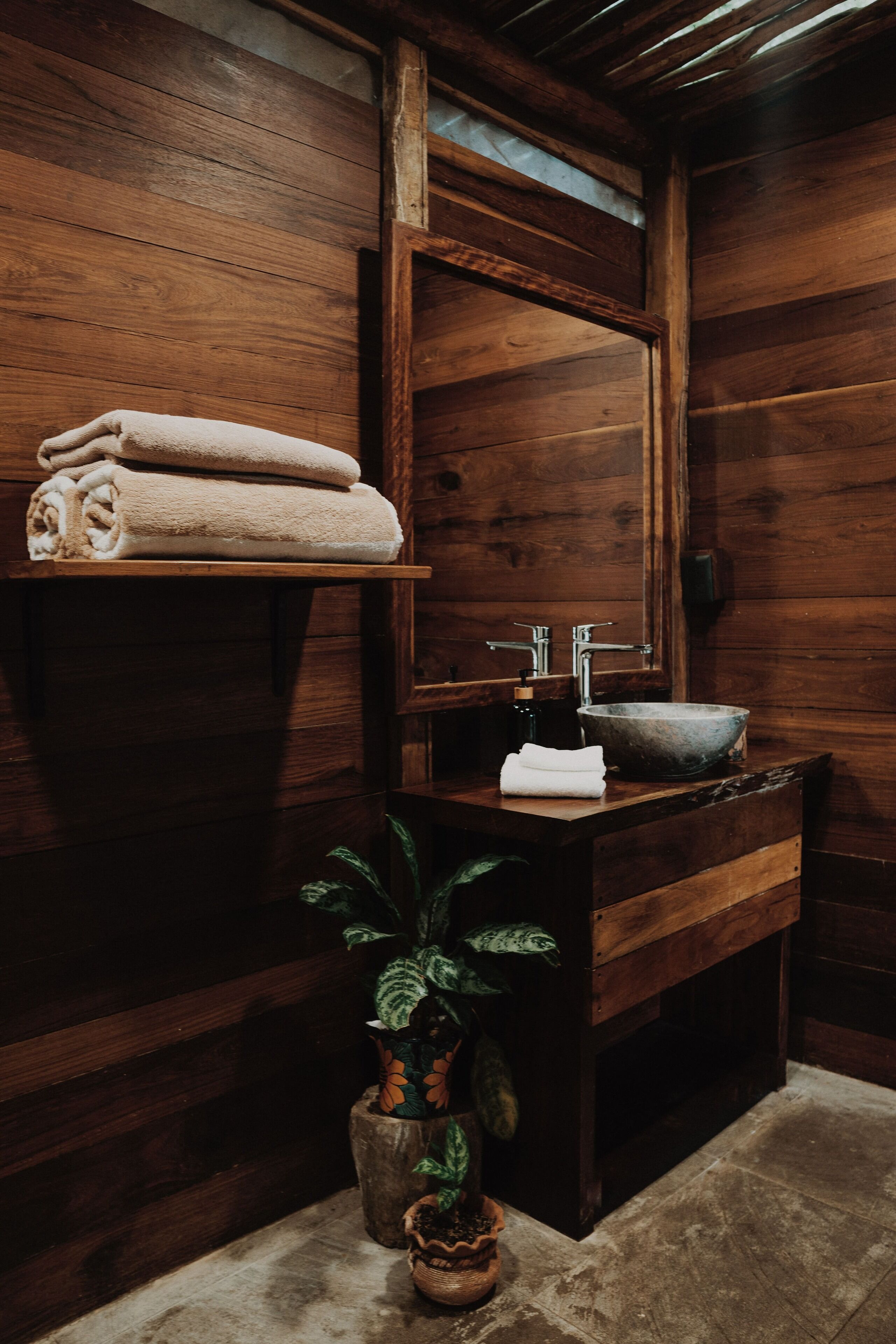 A wooden bathroom with a wooden sink, a mirror, and a shelf with folded towels.