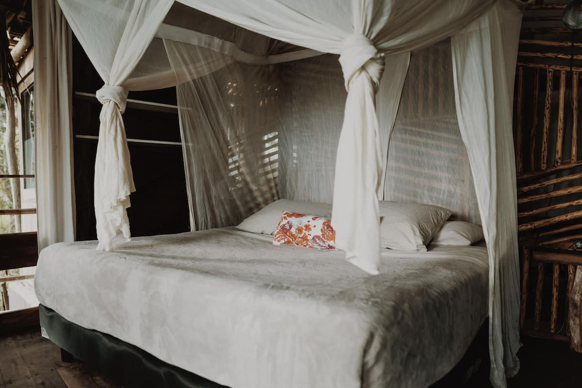 Una cama con dosel, un almohadón y una ventana con persianas.