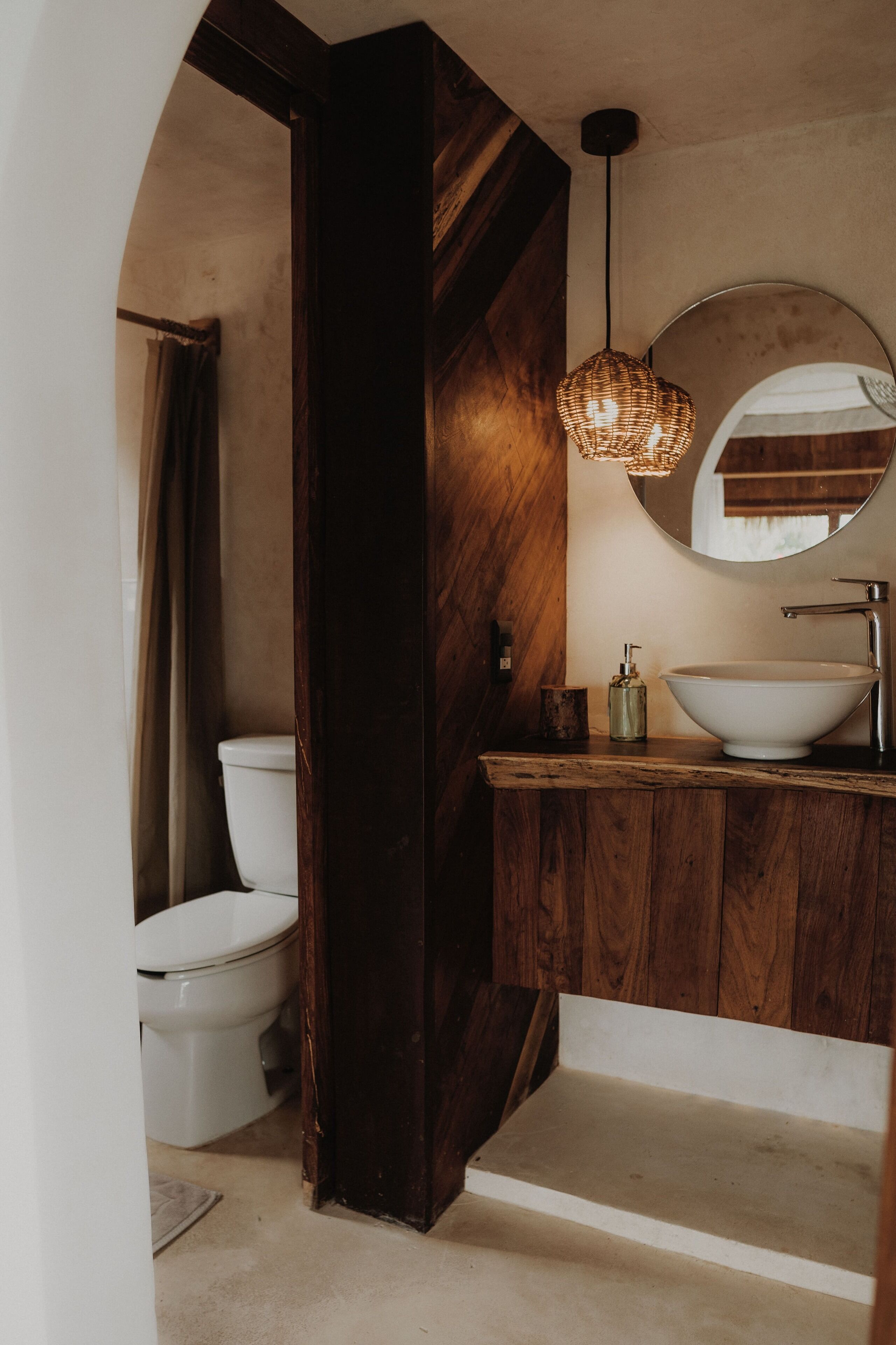 A bathroom with a wooden vanity, a round mirror, a white sink, and a hanging light fixture.