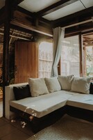 Una habitación de madera con sofá empotrado, ventana con cortinas y techo de paja.