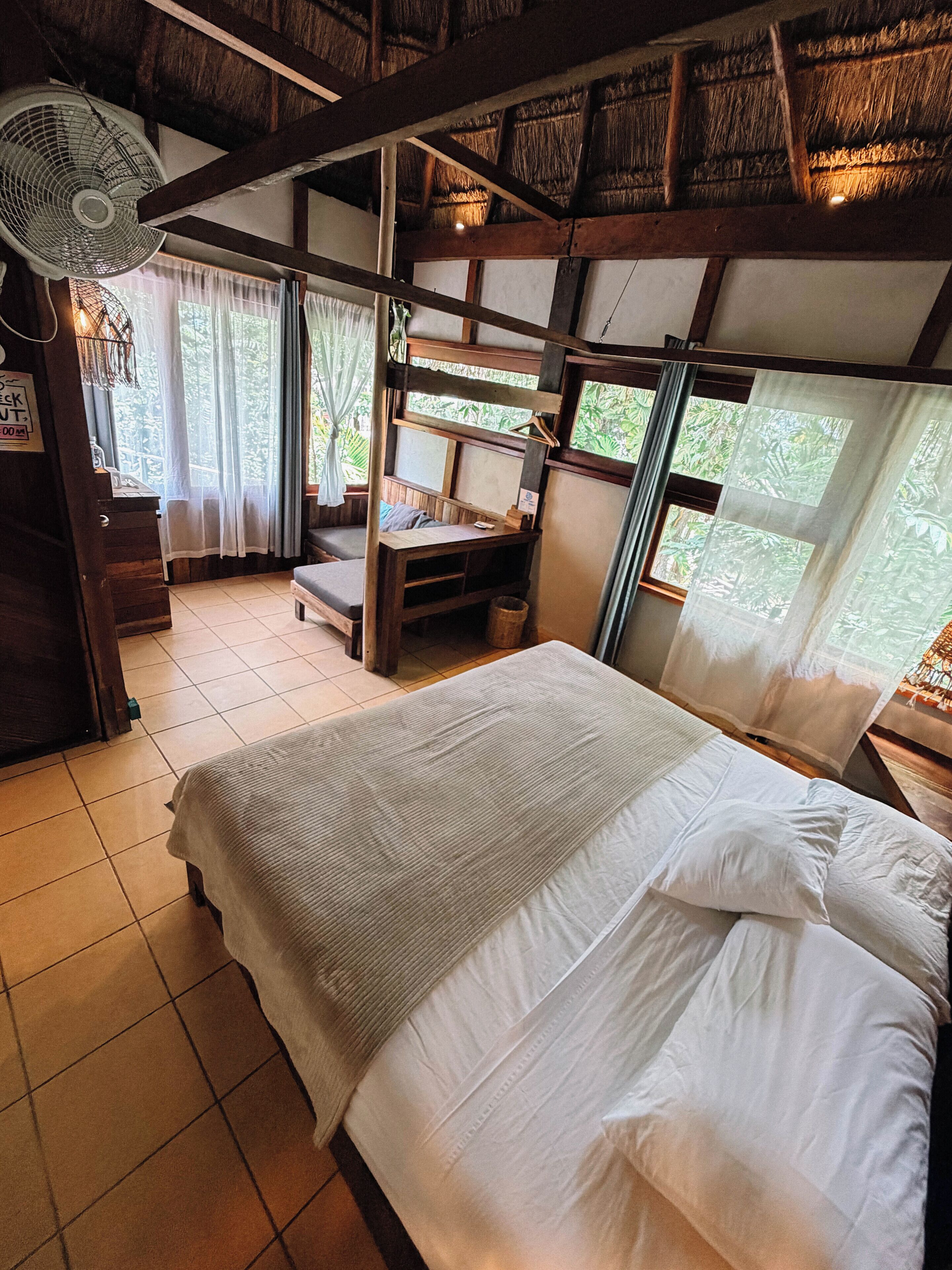 A room with a bed, a desk, and a fan.