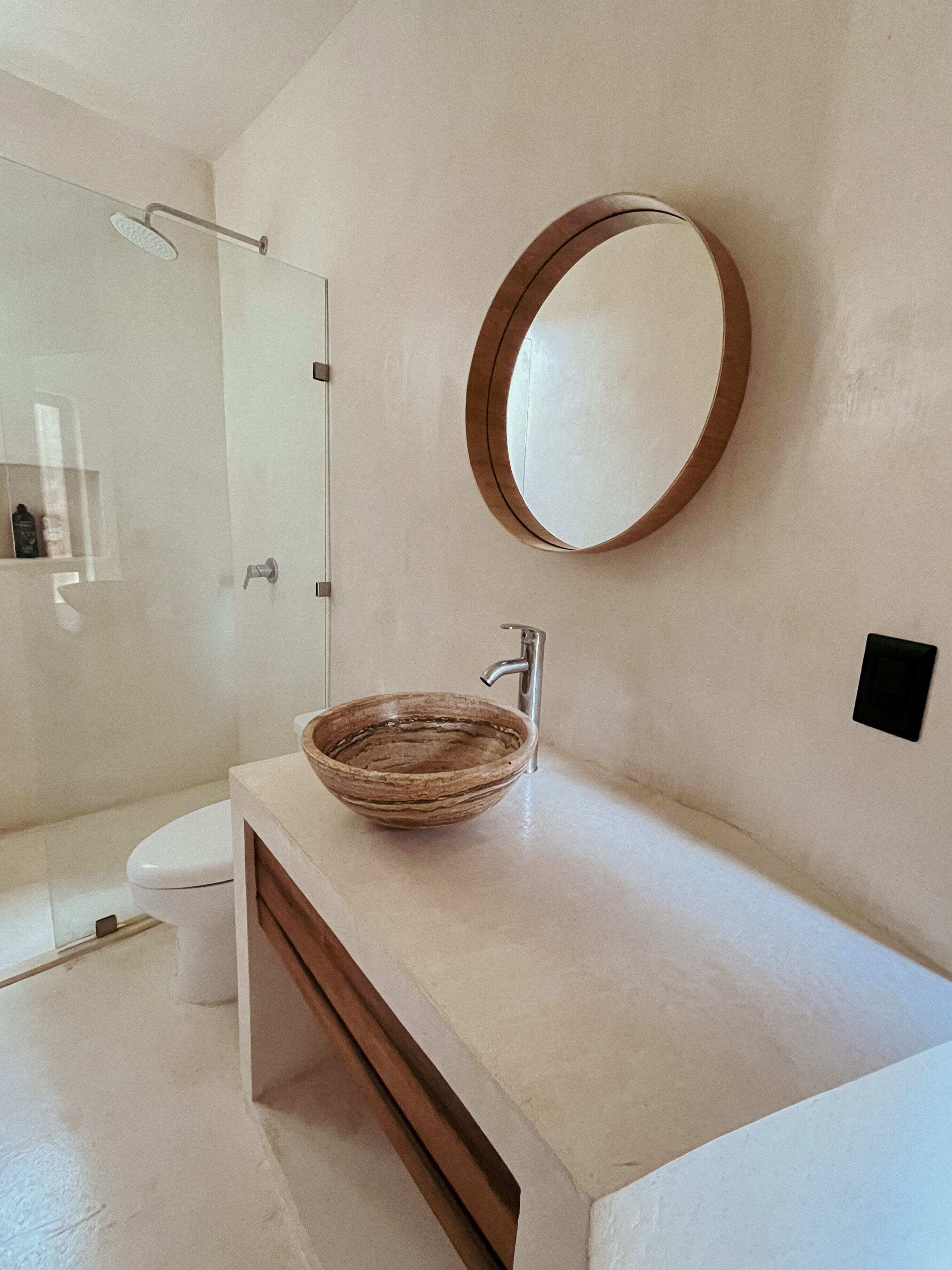 Une salle de bain avec un lavabo en forme de bol en bois, un miroir rond et une cabine de douche en verre.