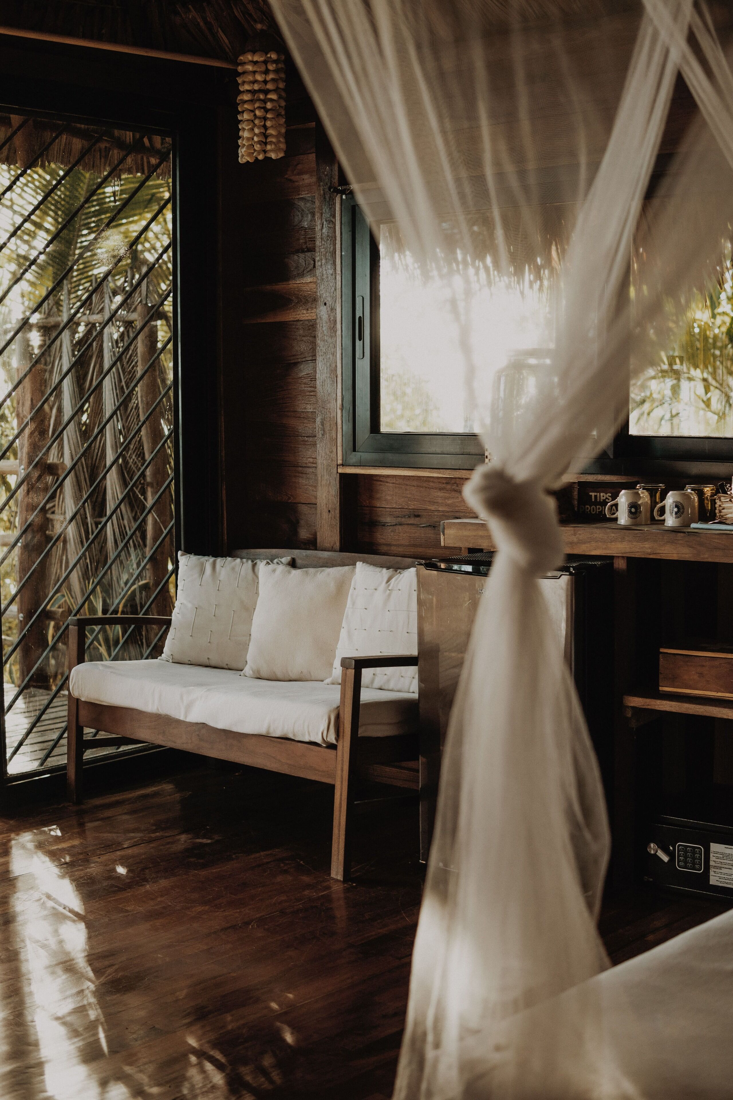 A wooden bench with cushions, a wooden desk with a radio, and a window with a view of palm trees.