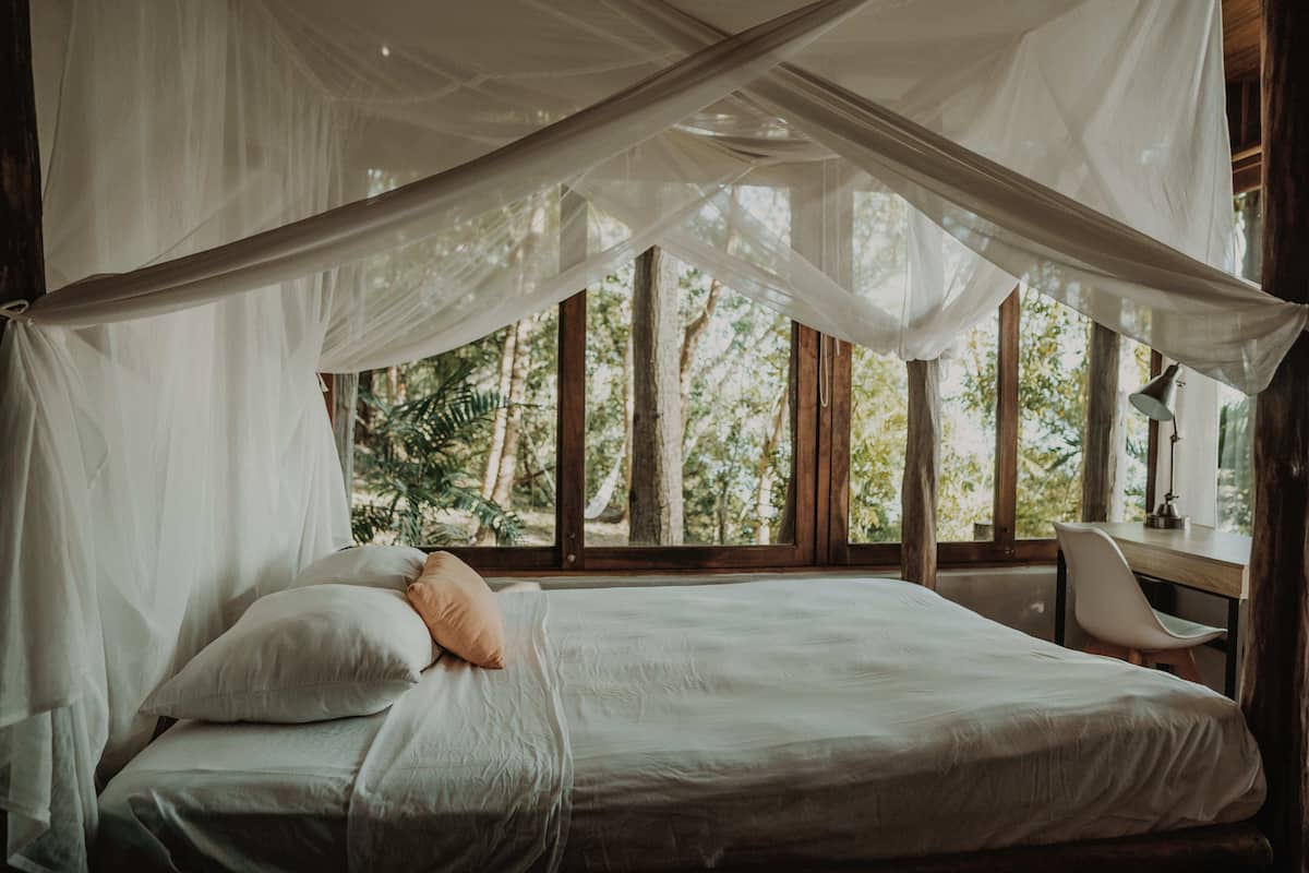 Una cama con dosel, un escritorio y una silla en una habitación con ventanas amplias.