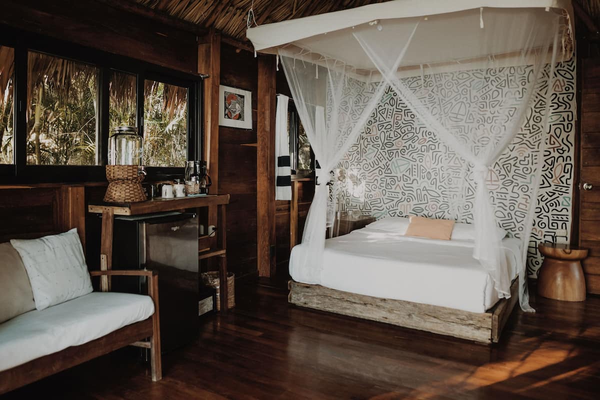 Una habitación de madera con una cama bajo un dosel, un sofá y una estantería con varios objetos.
