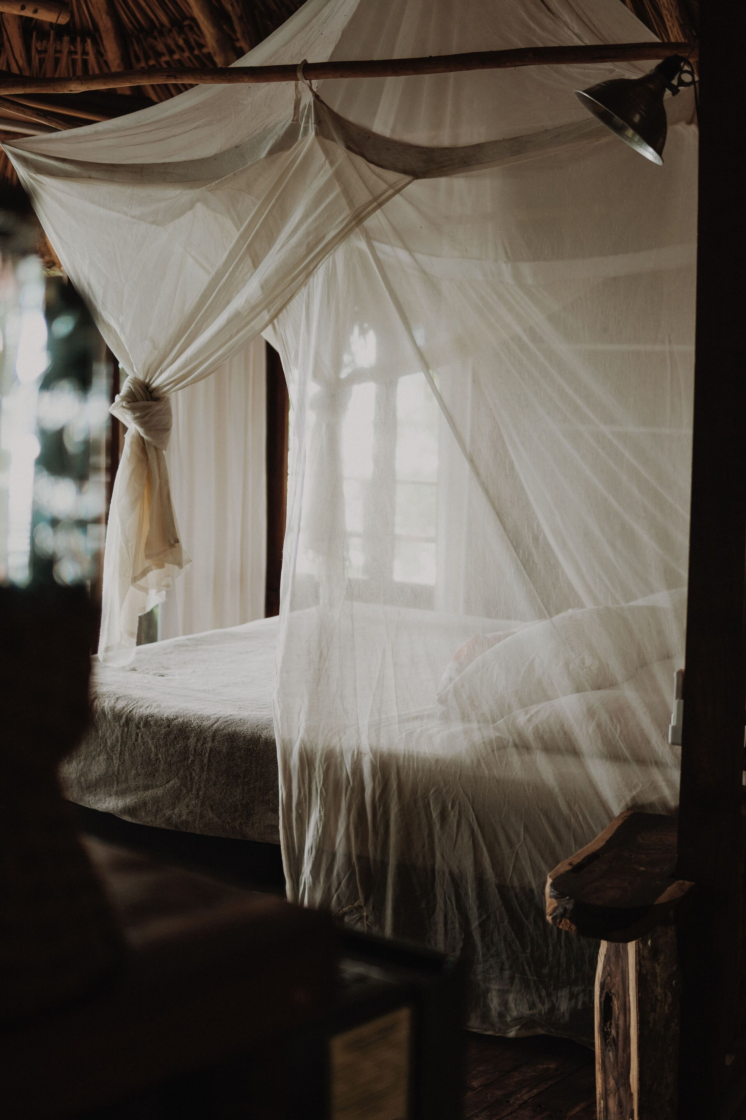 Ein Bett mit Baldachin, ein Holzstuhl und ein Fenster mit Tageslicht.