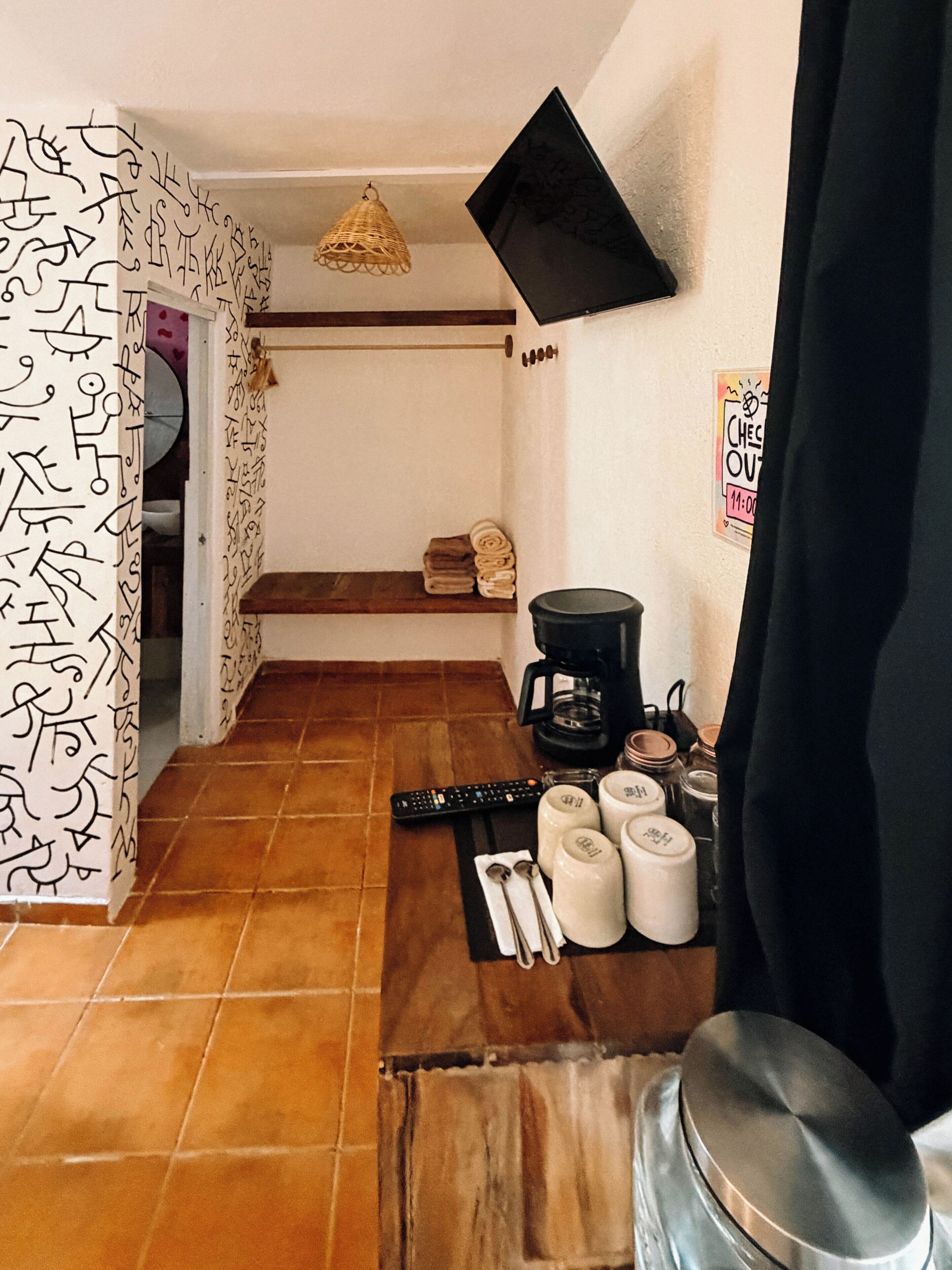 A kitchen with a coffee maker, utensils, and a TV mounted on the wall.