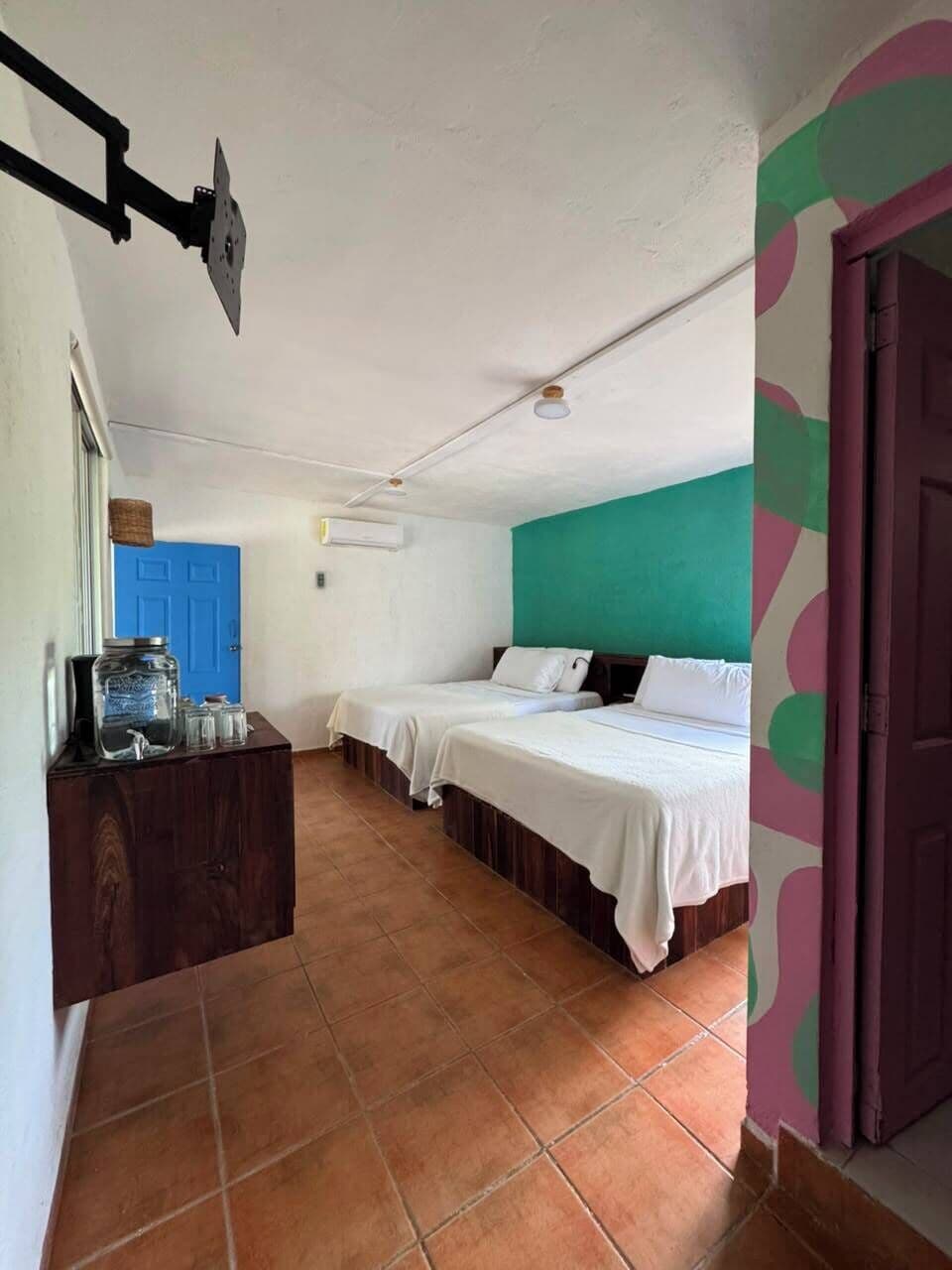 A room with two beds, a blue door, a wooden dresser, and a ceiling fan.