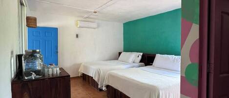 A room with two beds, a blue door, a wooden dresser, and a ceiling fan.