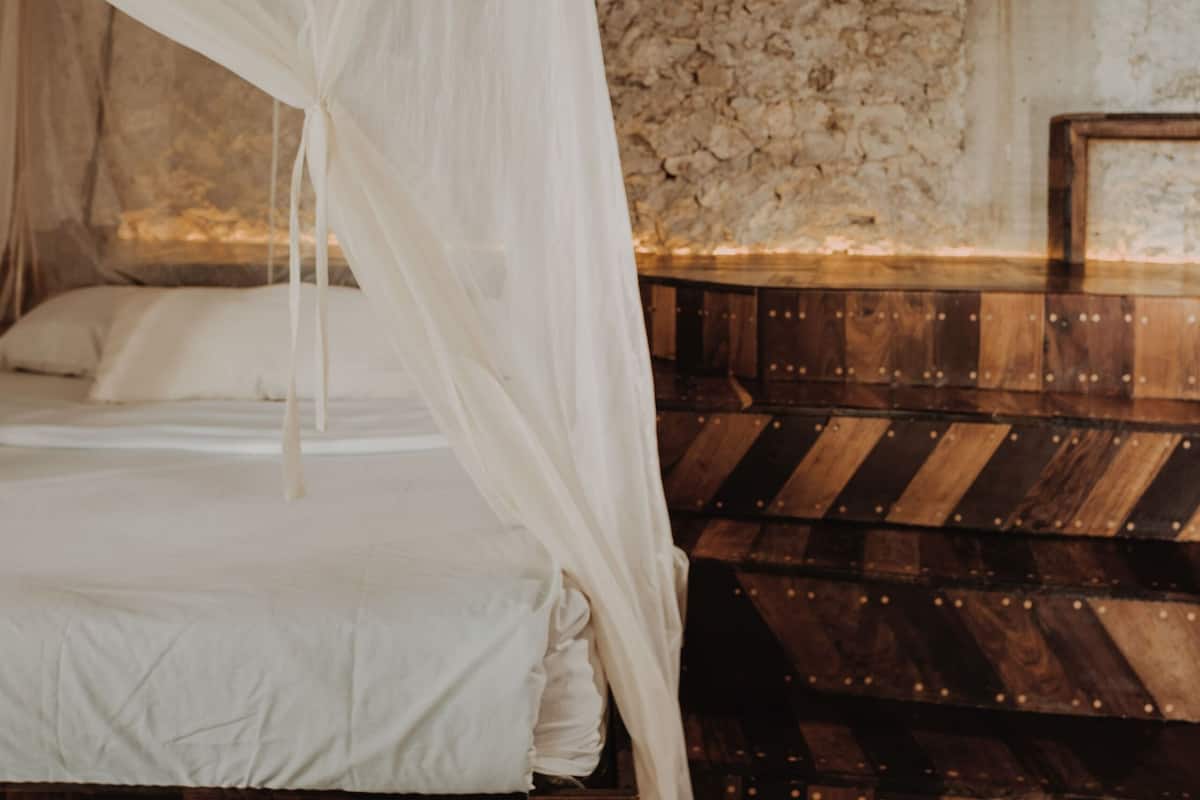 Una cama con dosel blanco, paneles de madera y pared de piedra.