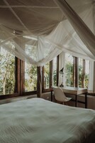 Un dormitorio con cama, escritorio y silla. Hay ventanas grandes con cortinas.