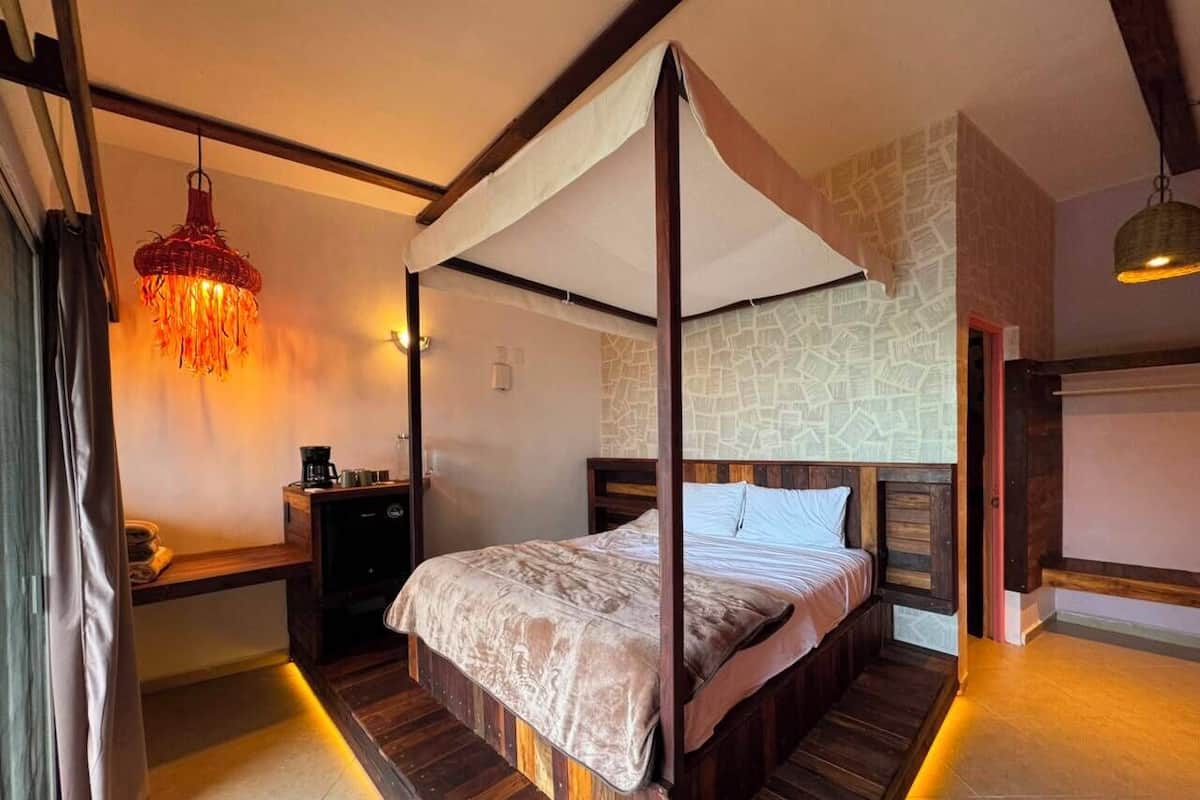 Una cama con dosel y cortinas, una mesita de noche con lámpara, y una pared con diseño de mapa.