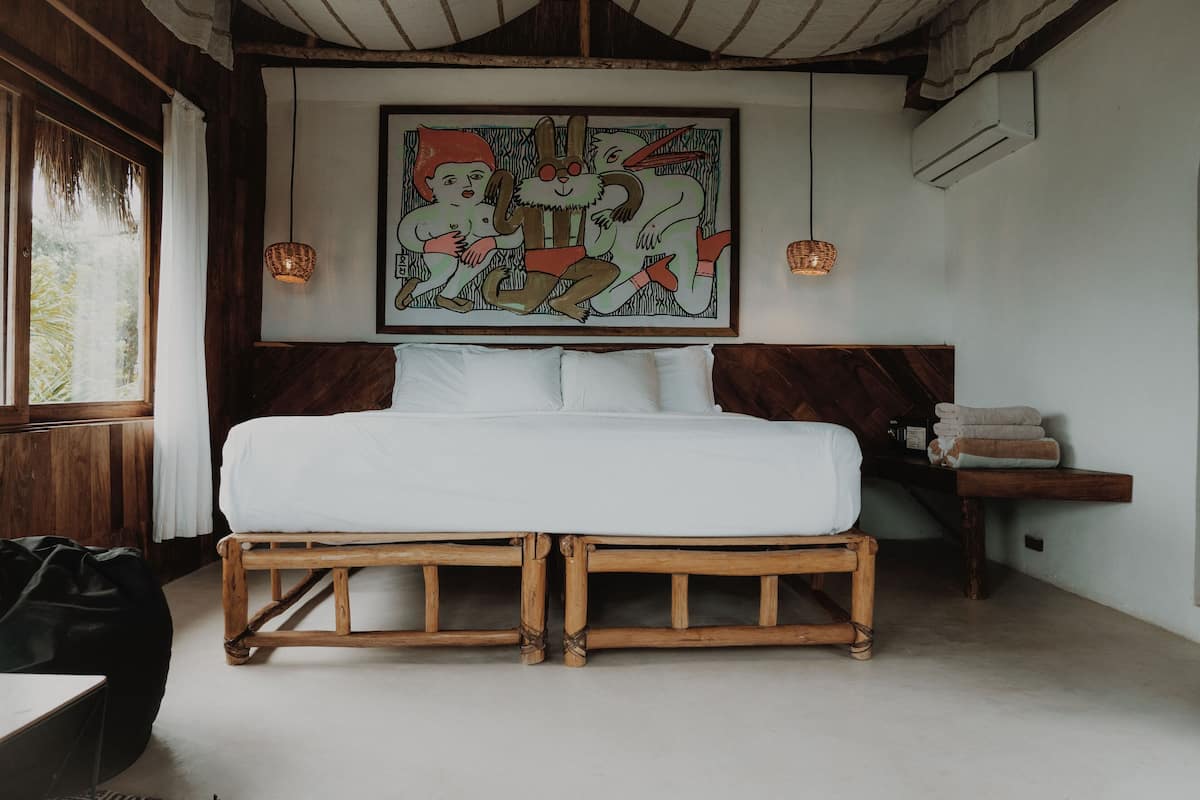 Una cama con estructura de madera y ropa de cama blanca en una habitación con un cuadro grande en la pared y dos luces fijadas a la pared.