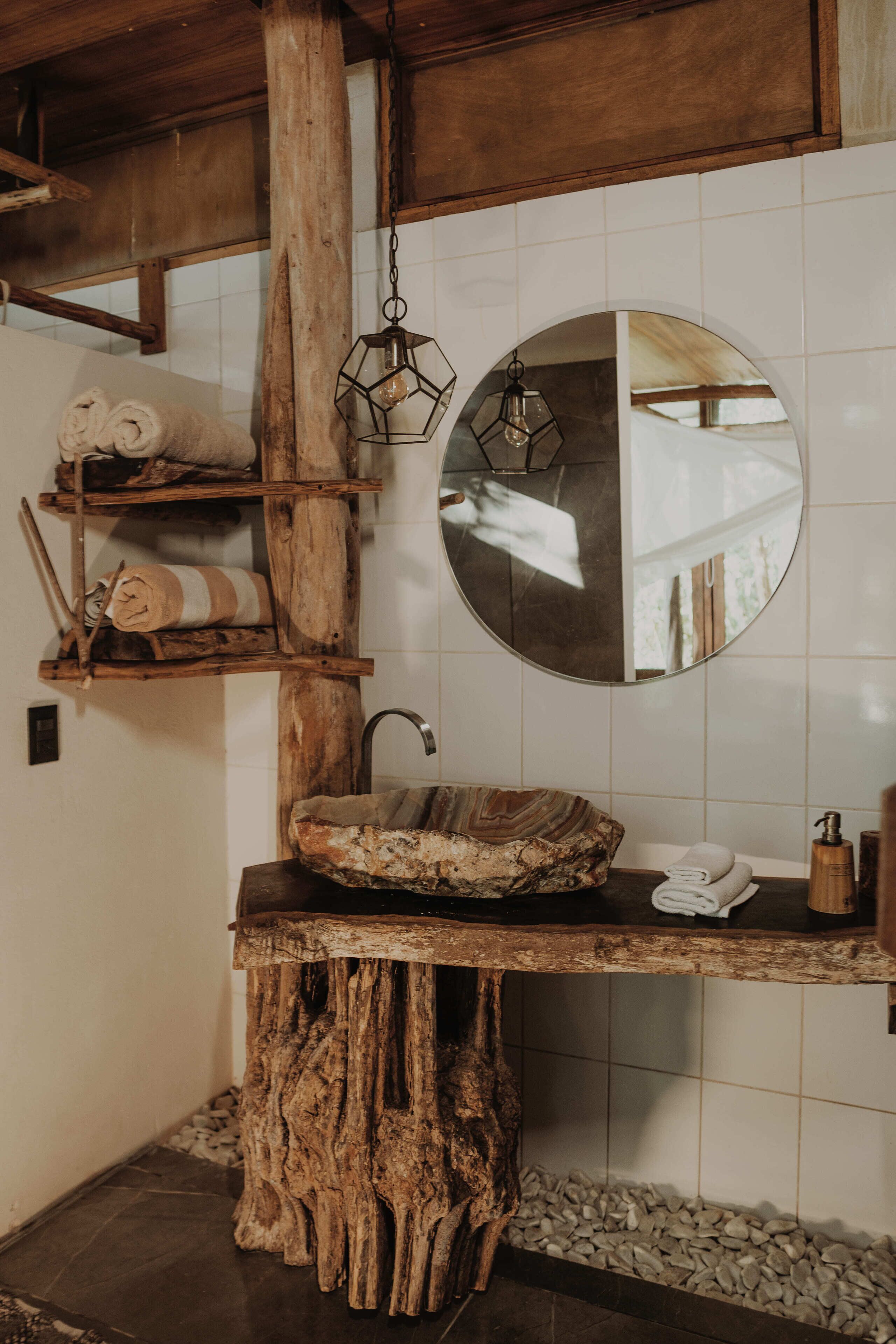 Un baño rústico con un lavabo de madera, un espejo redondo y repisas con toallas.