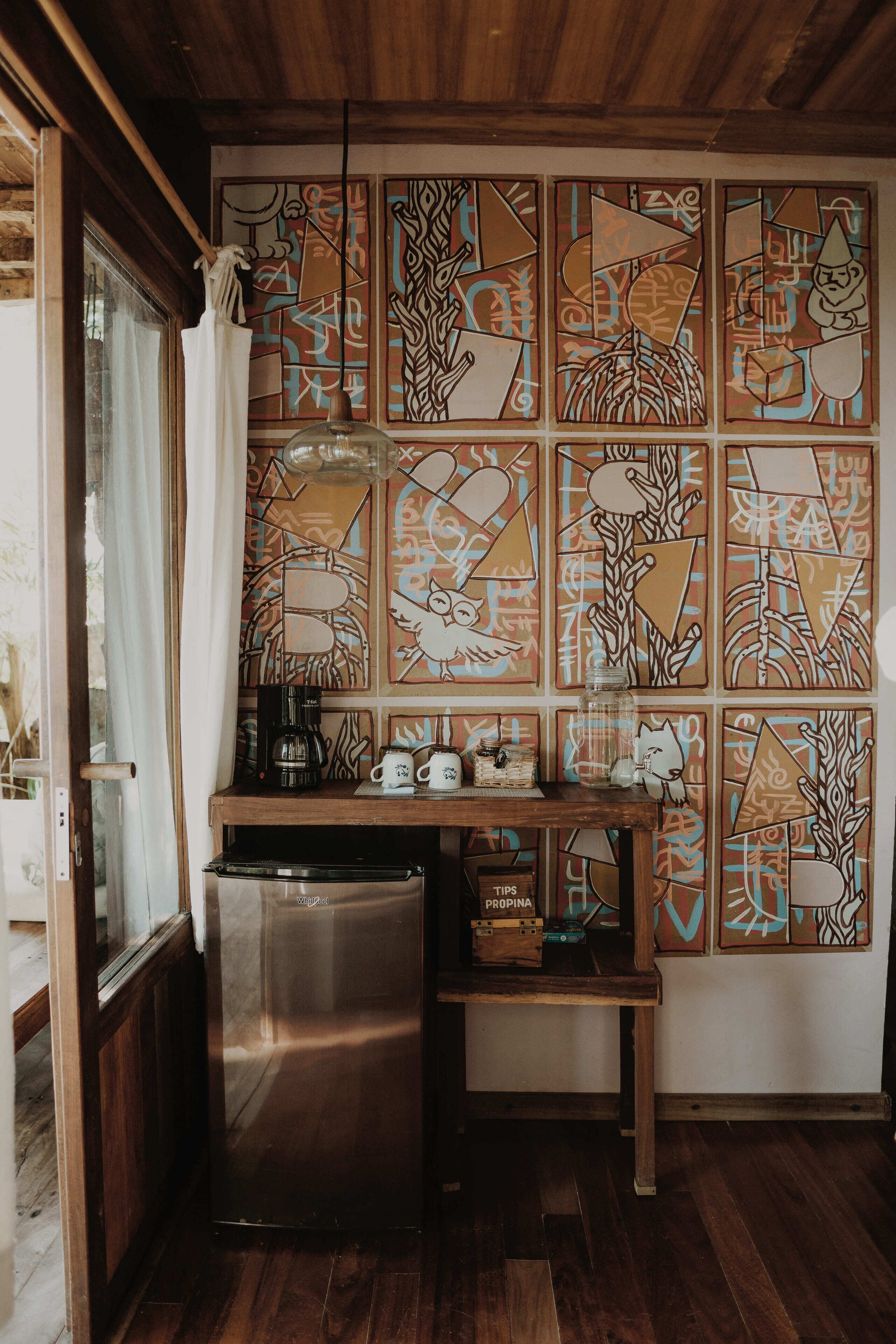 A compact kitchen with a stainless steel refrigerator, a coffee maker, and a shelf with a box labeled "PROPINA".