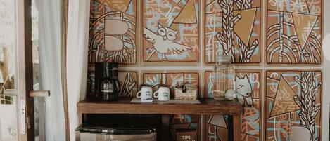 A compact kitchen with a stainless steel refrigerator, a coffee maker, and a shelf with a box labeled "PROPINA".