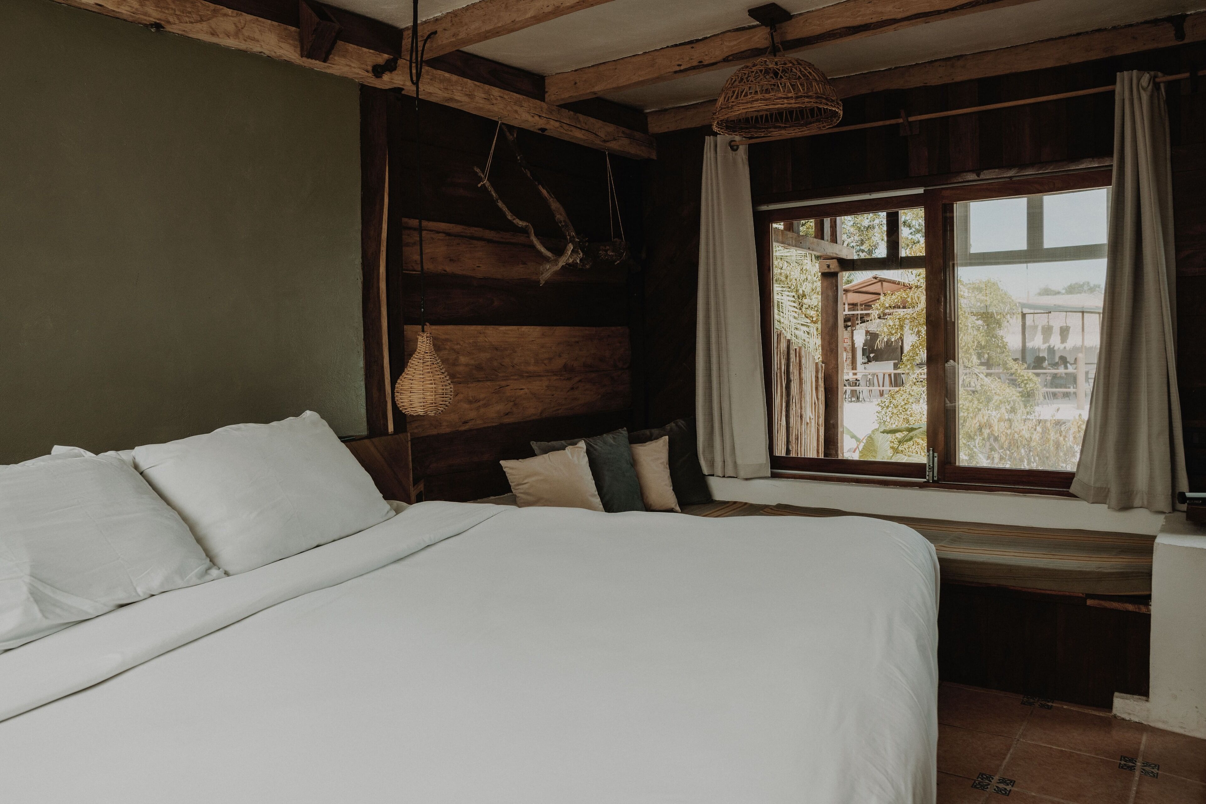 Un dormitorio con una cama grande, vigas de madera, una lámpara colgante y una ventana con cortinas.