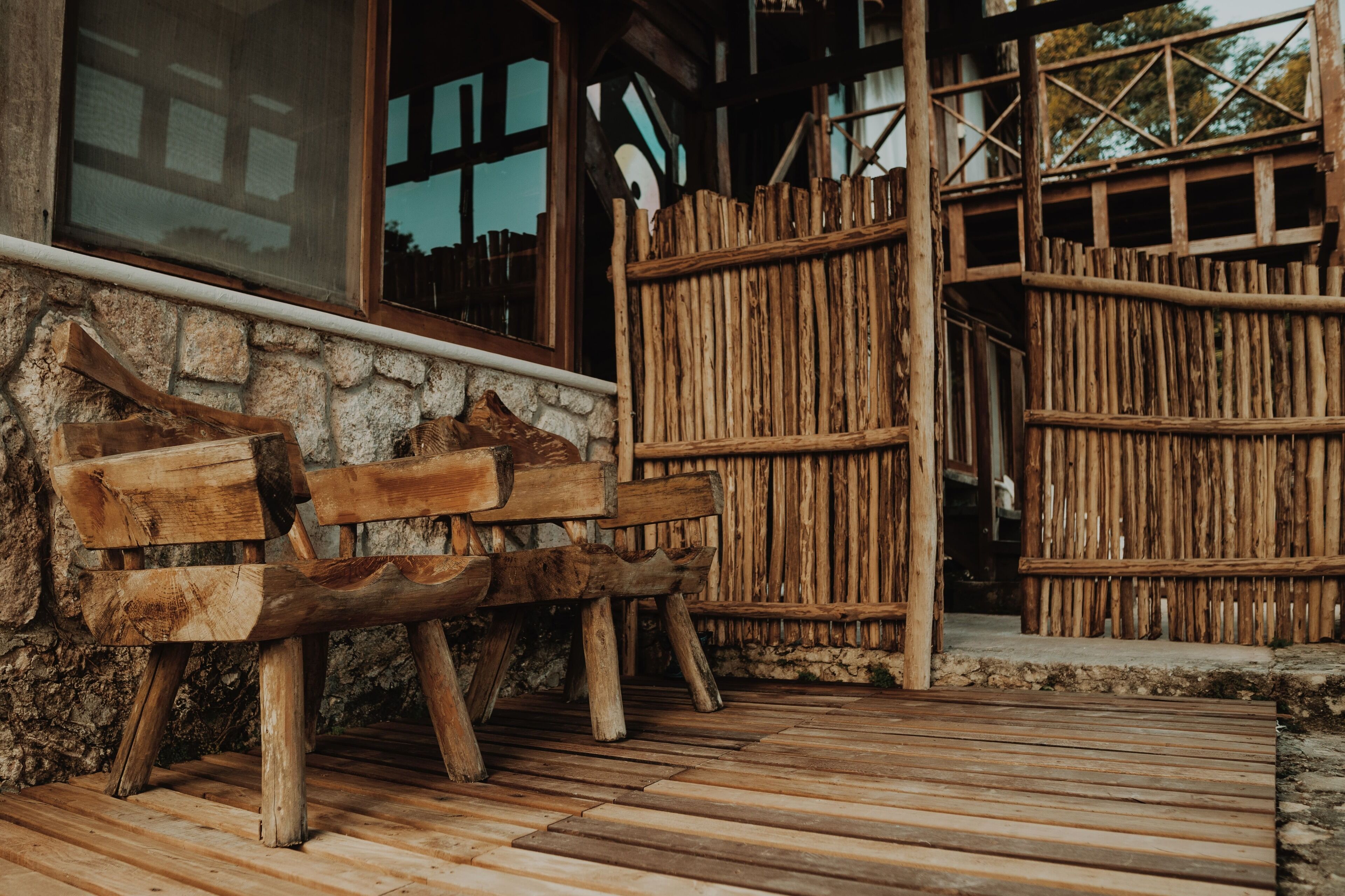 Un banc en bois rustique se trouve à l’extérieur d’un bâtiment doté d’un mur en pierre et d’une clôture en bois.