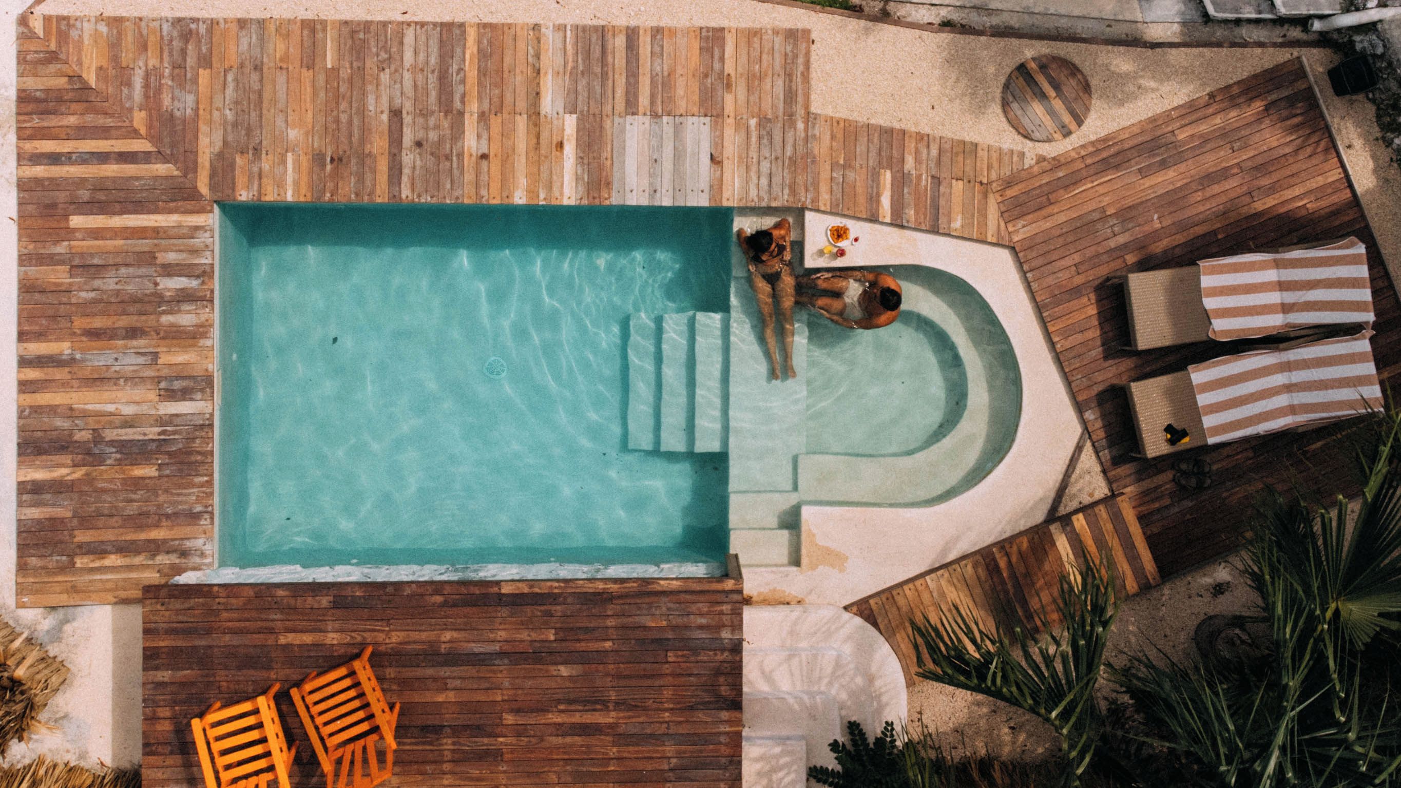 Vista aérea de una piscina con terraza de madera y sillas de descanso.