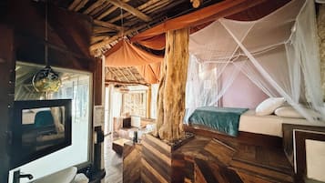 A rustic room with a bed, a wooden bench, a sink, and a window with curtains.