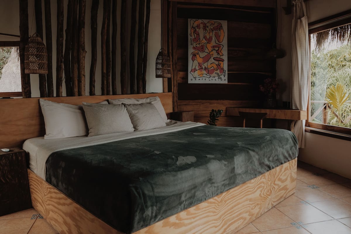 Una cama de madera con colcha verde, cabecero de listones verticales y un cuadro en la pared.