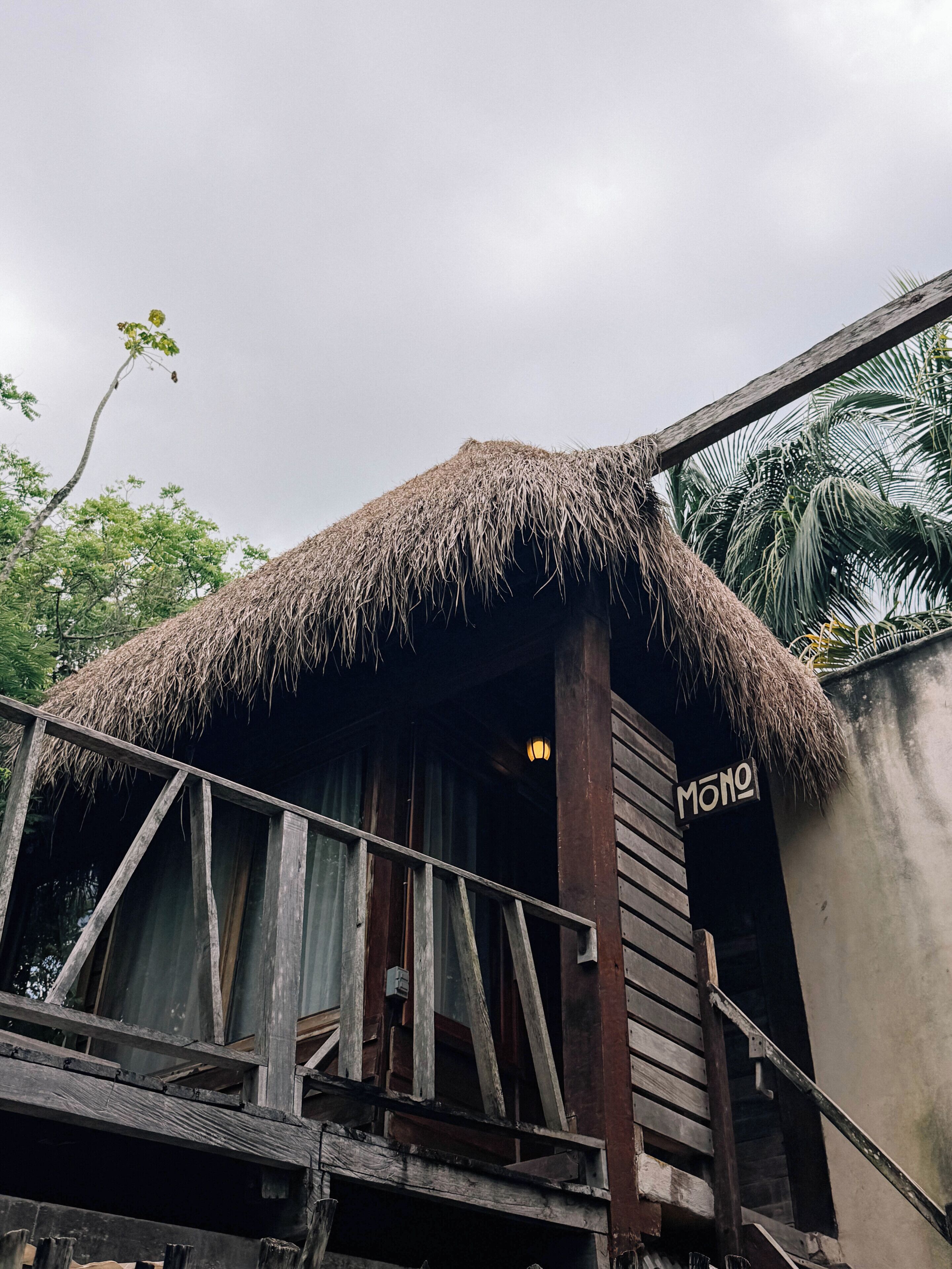 A wooden structure with a thatched roof, a sign reading 'MONO', and a staircase leading up to it.