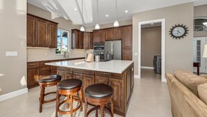 A modern kitchen with wooden cabinets, a large island with stools, stainless steel appliances, pendant lighting, and a clock on the wall. - Dockside Shore- Waterfront Home in Bayshore Arts District of Naples (Naples)