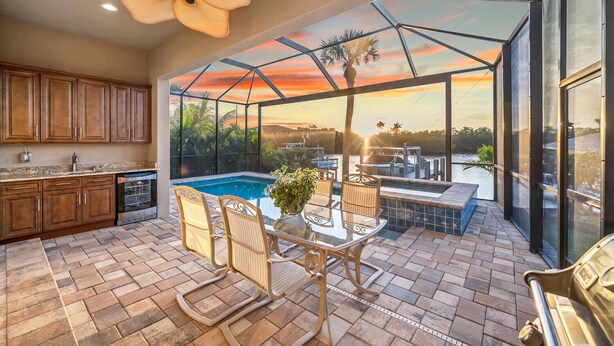 A spacious patio with a glass enclosure, a pool, and a dining area with outdoor furniture. - Dockside Shore- Waterfront Home in Bayshore Arts District of Naples (Naples)