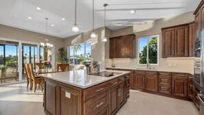 A spacious kitchen with a large island, wooden cabinets, and a view to the outside. - Dockside Shore- Waterfront Home in Bayshore Arts District of Naples (Naples)