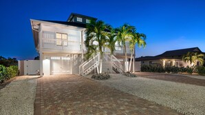 A modern two-story house with a covered driveway, palm trees, and a well-maintained garden.