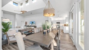 A spacious kitchen with white cabinets, a wooden dining table, and a large window.