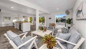 A spacious living area with a kitchen, dining area, and a view of the outdoor pool.