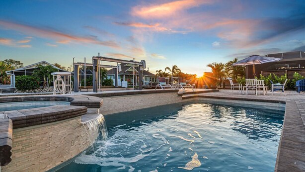 A swimming pool with a waterfall feature, lounge chairs, and a covered seating area.