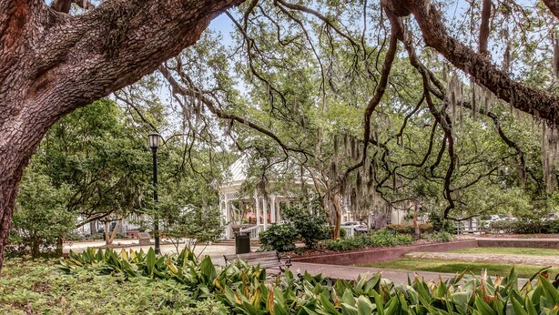A park with mature trees, a gazebo, and a paved walkway.